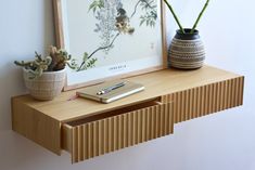 a wooden shelf with two plants and a book on it next to a framed print