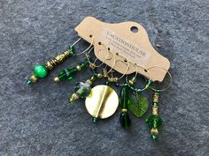 the green and gold earrings are attached to an earring that is hanging from a wooden hanger