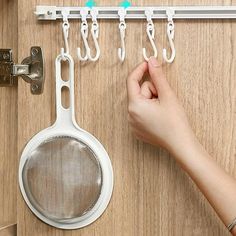 a person's hand is holding a strainer and hanging hooks on a door