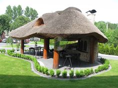 a thatched roof gazebo in the middle of a lawn with tables and chairs