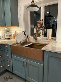 a kitchen with blue cabinets and an old fashioned sink in the center is decorated with copper knobs