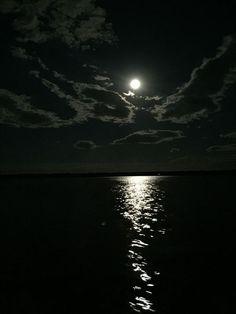 the moon shines brightly in the dark night sky over the water's surface