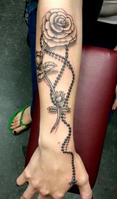 a woman's arm with a rose and rosary tattoo on it