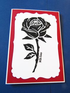 a red and white card with a black rose on the front, sitting on a blue surface