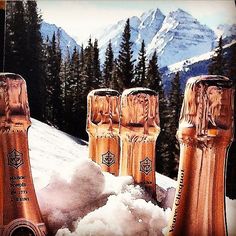 three champagne bottles in the snow with mountains in the back ground and trees behind them