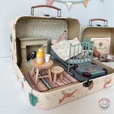 an open suitcase filled with furniture and toys on top of a white table next to a wall