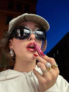 a woman wearing sunglasses and a hat is holding a lipstick