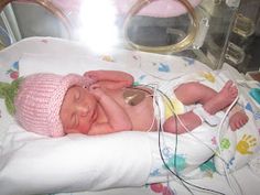 a baby in a pink hat laying on top of a bed next to a hair dryer