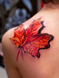 the back of a woman's shoulder with a colorful leaf tattoo on her left shoulder