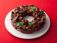 a chocolate doughnut with nuts and cherries on a white plate against a red background