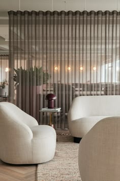 a living room with two white chairs and a round glass table in front of a sheer curtain