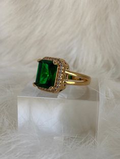 Talk about green with envy! The Emerald Sage Block Ring is one of this seasons most desired rings. This jewel features a radiant cut emerald CZ, about 13 mm H x 12mm W, showcased within a cubic zirconia encrusted frame and is secured on a split smooth open band. The green-eyed monster is bound to appear when rocking this gal! Mix and match with these emerald embellished jewels! - The Jeweled Emerald Necklace - The Emerald Jade Pendant Necklace - The Verdi Emerald Ring Available in 24K gold or rhodium plating over steel Patent plating & sealant technology to ensure durability and long lasting wear Made in Los Angeles, CA | Nickel & Lead Free Emerald Green Stone Ring, Gold Ring Stone Design, Green Emerald Ring Gold, Emerald Green And Gold Jewelry, Gold Jwelery Designs, Green Stone Gold Ring, Gold And Emerald Ring, Emerald Design, Jewellery Essentials