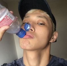 a young man wearing a hat drinking from a plastic water bottle while wearing a baseball cap