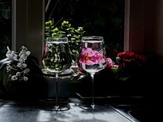 two wine glasses sitting on top of a table with flowers in the window sill