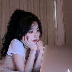 a woman laying on top of a bed with a laptop computer next to her face