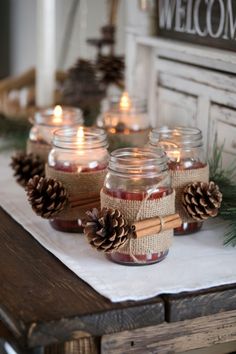 mason jars filled with candles sitting on top of a wooden table next to pine cones