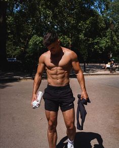 a shirtless man walking down the street with no shirt on, holding an object in his hand