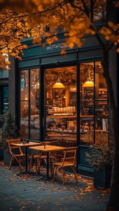 an outdoor cafe with tables and chairs in front of the store windows at night time