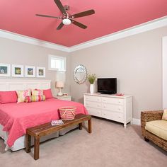 a bedroom with pink and yellow accents, white furniture and a flat screen tv on the wall