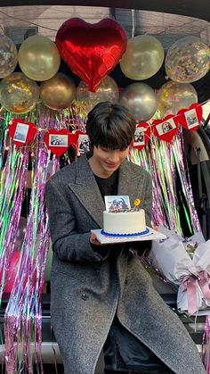 a man holding a cake in front of balloons and streamers on the back of a car