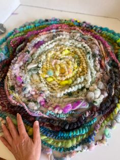 a person's hand is pointing at a pile of yarn on a white table