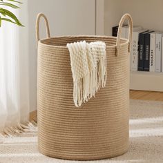 a large round storage basket with tassels on the handles and bottom, in front of a bookshelf