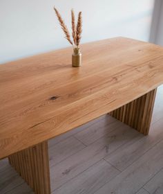 a wooden table with two vases on it and some grass in the middle, against a white wall