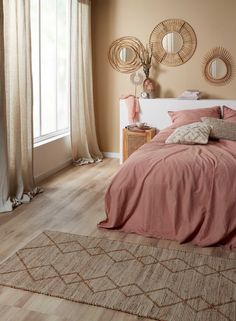 a bed sitting in a bedroom next to a window covered in pink sheets and pillows