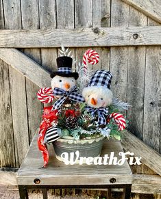 two snowmen sitting on top of a potted plant in front of a wooden fence