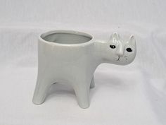 a white ceramic cat shaped cup on a white tablecloth with the lid open to show it's face