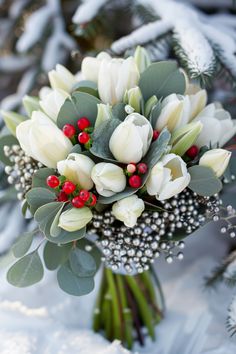 a bridal bouquet with white tulips and red berries sits in the snow