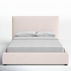 a bed with two pillows on top of it and a white wall in the background