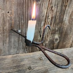 a candle is being held by a pair of scissors on a piece of wood,