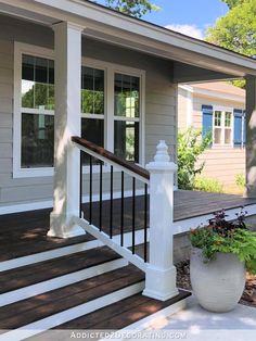 a porch with white railing and planters on the front steps, next to a gray house