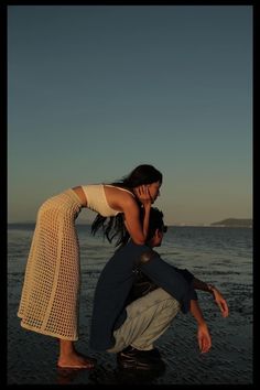 two people standing on the beach and one is talking on a cell phone