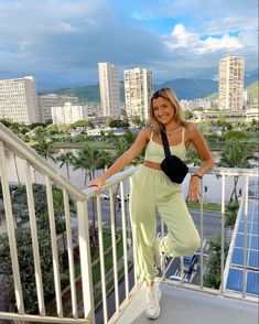 a woman standing on top of a balcony next to a metal railing with buildings in the background