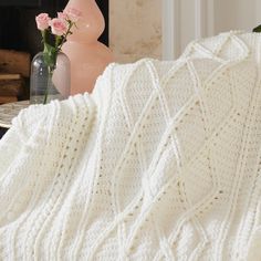 a white crocheted blanket sitting on top of a table next to a vase with flowers