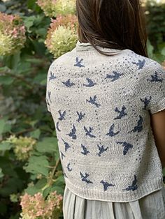 the back of a woman's sweater with birds on it and flowers in the background