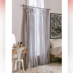 a bedroom with a bed, desk and window curtained in white sheer curtains on the windowsill