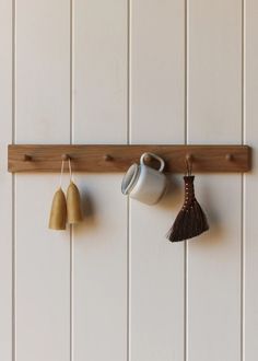 two mugs, one with a tassel and the other with a broom hanging on a wall