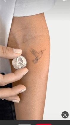 a woman's arm with a small bird tattoo on it and a coin in the foreground