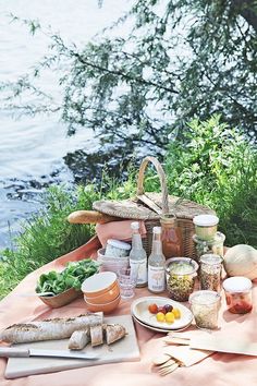 a picnic table with bread, vegetables and condiments on it next to the water