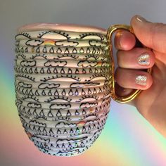 a hand holding a coffee mug with designs on the outside and gold trimmings