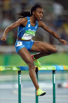 a female athlete is jumping over a hurdle