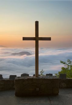 a wooden cross sitting on top of a stone wall next to a fog covered mountain