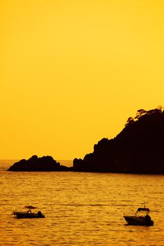 two boats floating in the ocean at sunset