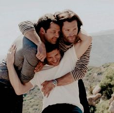 three men hugging each other on top of a mountain