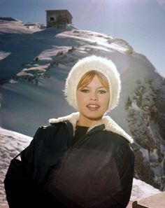 a woman standing on top of a snow covered slope next to a mountain with a building in the background