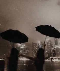 two people holding open umbrellas in front of a cityscape at night time