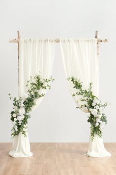 two white curtains with flowers and greenery in front of them on a wooden floor